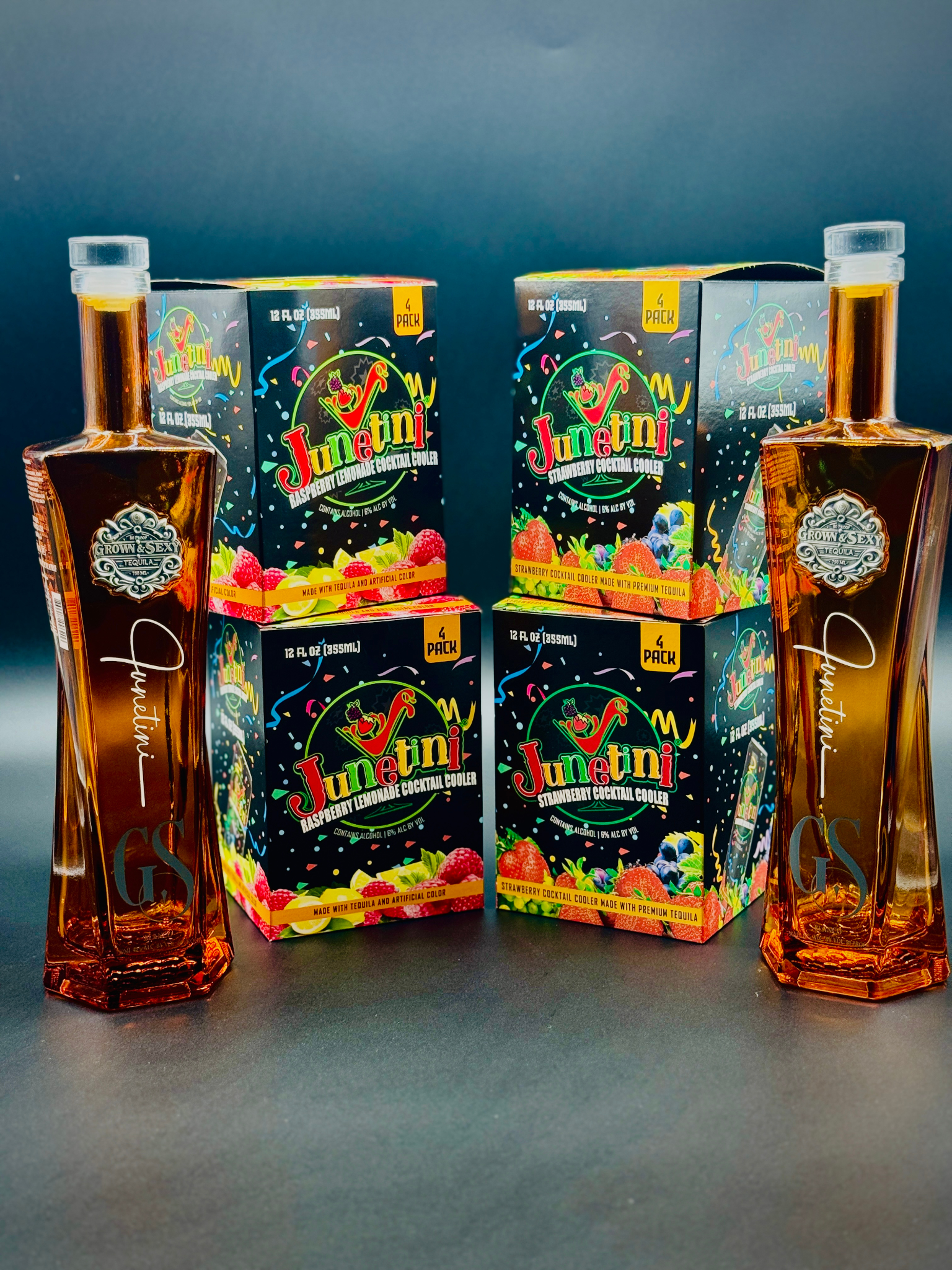 Two bottles of Grown & Sexy tequila with boxes of Junetini Raspberry Lemonade and Strawberry Cocktail Coolers on a dark background
